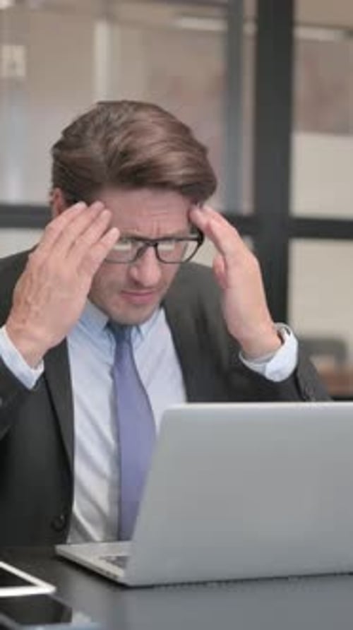 Businessman having Headache while Working on Laptop in Office, vertical