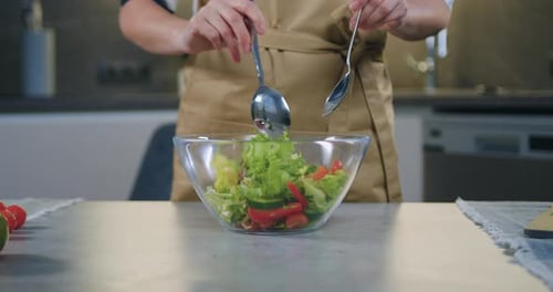 Close up woman hands hold spoons and mixing refreshing vegetable salad in glass bowl for dinner