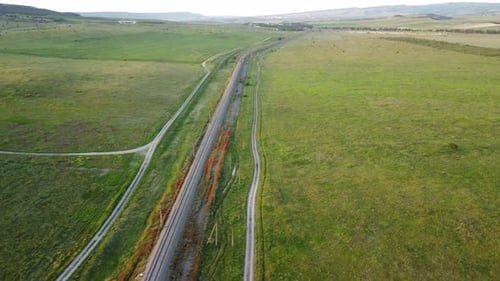 Luftaufnahme einer Eisenbahnstrecke, die durch ein üppiges Feld mit grünem Weizen auf dem Land führt