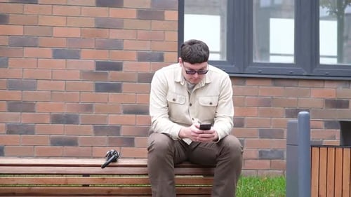 Man Sitting on Bench Using Phone Outdoors