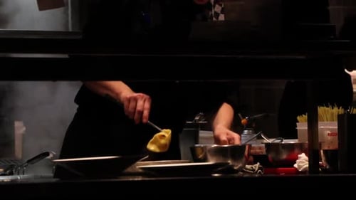 Chef serving pasta from a bowl on a plate in a professional restaurant kitchen in slow motion