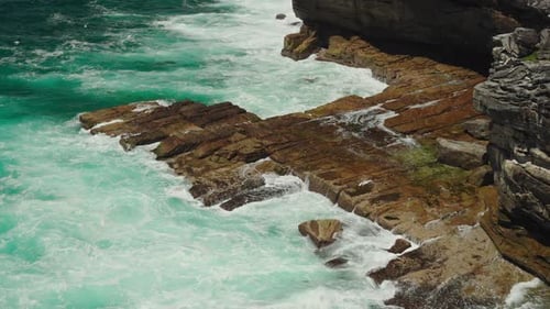 A Rugged Ocean Shoreline Where Powerful Waves Crash Against Weathered Rocks Creating Swirling Foam