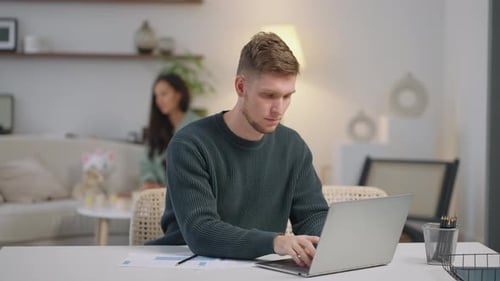 A Business Woman Works Remotely at Home on a Laptop and Shows Graphs on a Webcam While the Family is