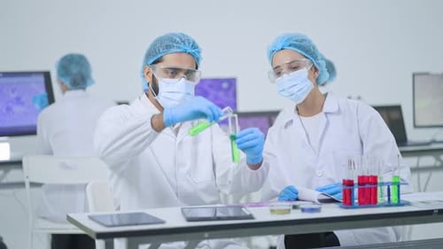Male researcher in mask and goggles holding two test tubes
