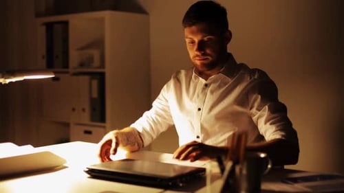 Man Working Late at Desk With Laptop and Pen