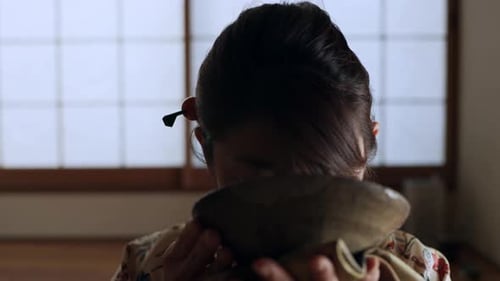 Mujer asiática disfruta de té caliente en una habitación tradicional japonesa con iluminación tenue