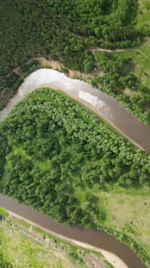 Aerial of Winding River Between Green Meadows and Forest Landscape with a Small Meandering River