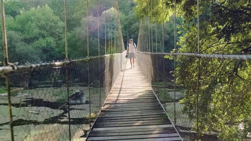 Caucasian male crossing suspension bridge over river calm water in national park, Slow motion