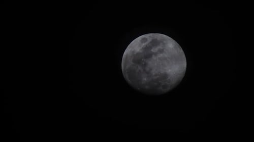 Aufnahme des aufgehenden Vollmonds mit Wolken vor dem Mond und schwarzem Hintergrund.
