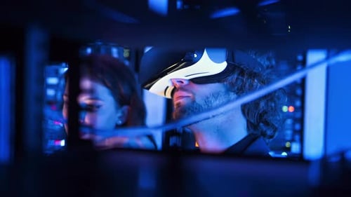 Woman programming in a server room while a man is using a Virtual Reality headset