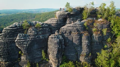 Hikers stand atop a rocky observation platform, gazing out over the expansive valley and forest.