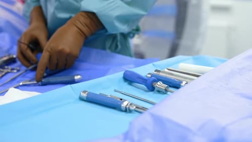 Unrecognized medic wearing brown latex gloves stands at the surgical stand with a range of tools.