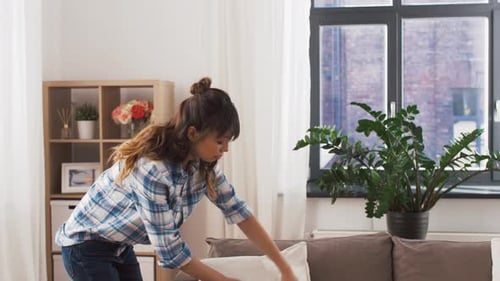 Asian woman arranging sofa cushions for a clean and happy home interior