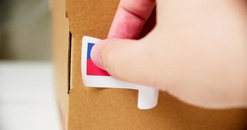 Hände, die das MADE IN TIWAN Flaggenetikett auf einem Versandkarton mit Produkten anbringen. Nahaufnahme mit