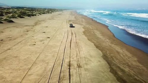 Truck driving on sandy beach next to ocean from Drone