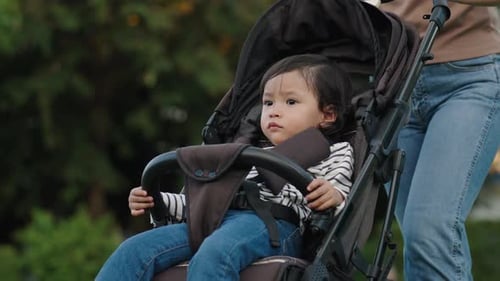 mother pushing toddler baby stroller and walking in the park