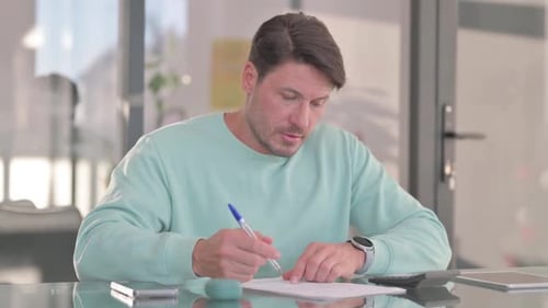 Man Writes at Desk in Bright Indoor Office