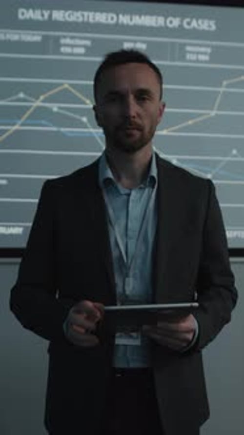 Man With Tablet Stands Before Data Graphics