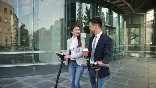Two business people with electric scooter talking outside in front of modern business building.
