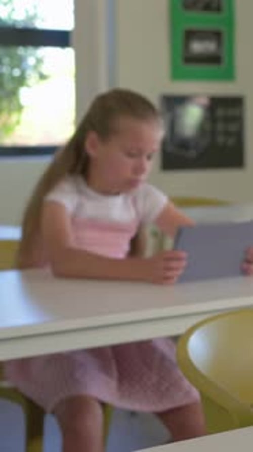 Vertical video: Shifting gaze student holding tablet at classroom desk, in white top and pink skirt