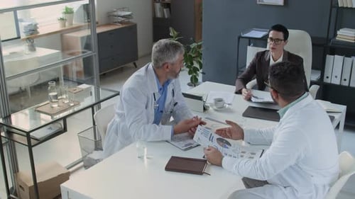 Group of Healthcare Professionals Discussing Reports at Meeting in Modern Office