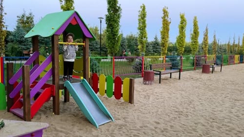 Lovely toddler in stripy jacket hanging on the horizontal bar at playground.