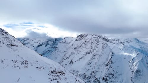 aerial drone view of a large mountain range covered in snow and clouds
