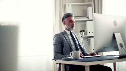 Businessman with Computer Sitting at the Table in an Office, Stretching Arms