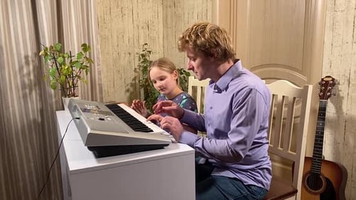 Man Plays Keyboard With Young Child Indoors