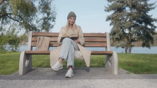 Woman Relaxing with a Book on a Park Bench in a Tranquil Outdoor Setting