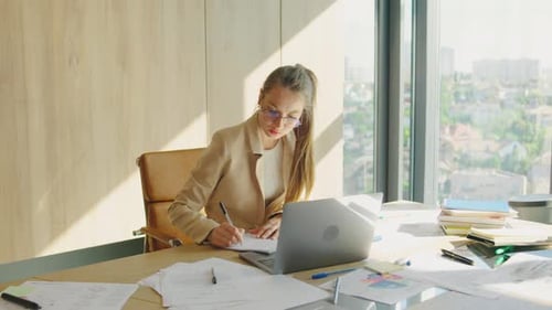 A Dedicated Businesswoman Focused on Work in a Modern Office with a Laptop and Documents She is