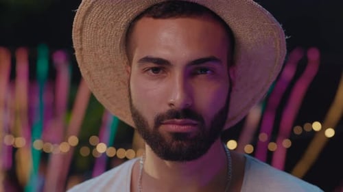 Smiling man with beard and hat points at camera