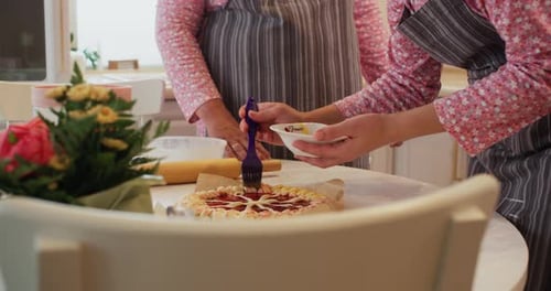 Woman is Covering Egg Icing Homemade Pie with Jam in Kitchen with Her Mom