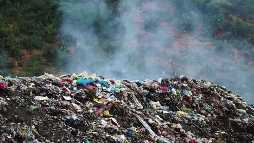 Stack of different types of large garbage dump, plastic bags, and trash burning near paddy rice terr