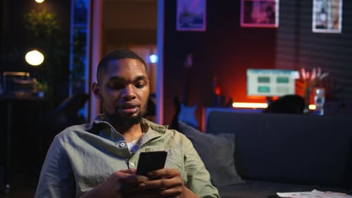 African American Young Guy Enjoying Break with His Phone on Sofa