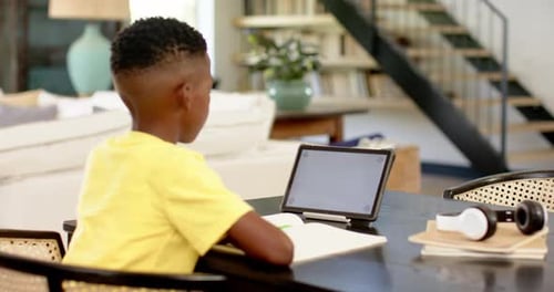 Boy studying at home using tablet and notebook, focusing on schoolwork, copy space