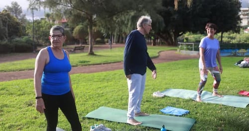 Senior People Doing Yoga Exercises Outdoor with City Park in Background -
