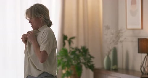 Woman Puts on Shirt in Bedroom