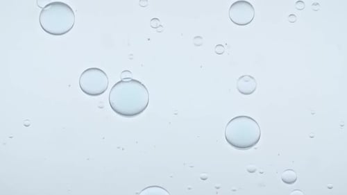 Bolhas azuis transparentes se formam e flutuam em direção a outras em uma superfície transparente sobre fundo azul O