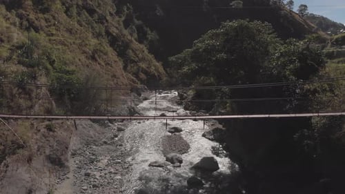 Metal wire suspension bridge spanning over river in remote wilderness terrain stationary medium wide