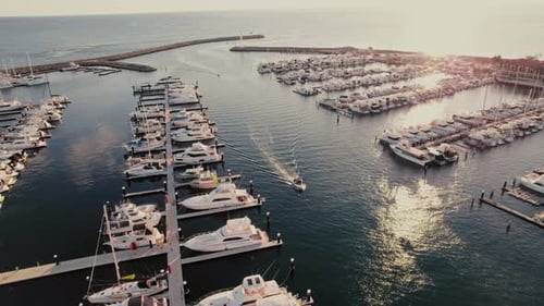 Scenic marina view at sunset with boats and yachts docked and a vessel cruising in the water