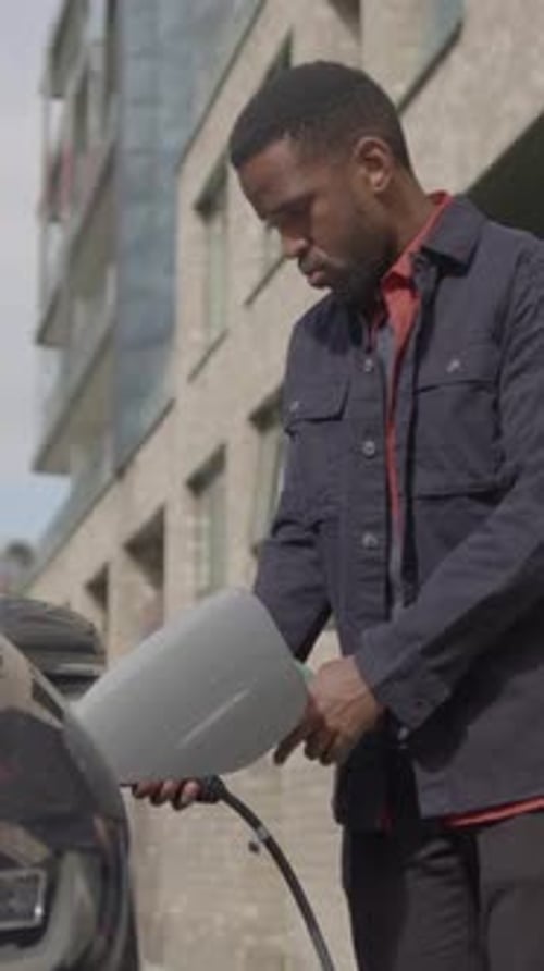 Businessman Charging Electric Car and using Smart Phone Technology