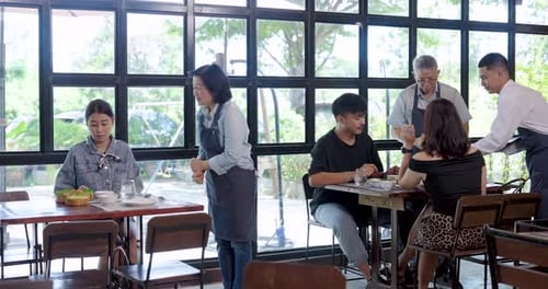 Asian senior couple cafe owners serving customers in bright restaurant interior, teamwork management