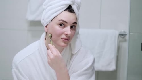 Woman Massaging Face with Facial Roller in Bathroom