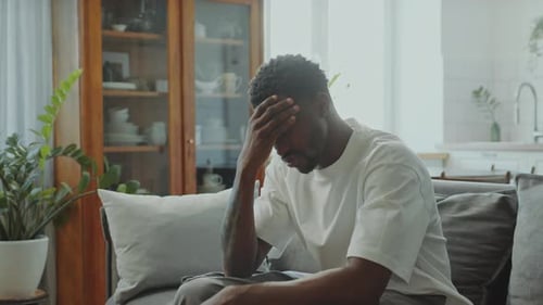 Man Sitting on Couch with Hand on Forehead
