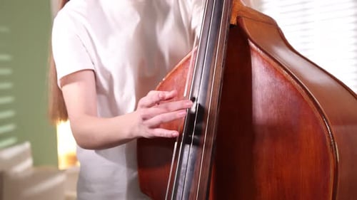 Woman Practices Playing Large String Bass Instrument Indoors