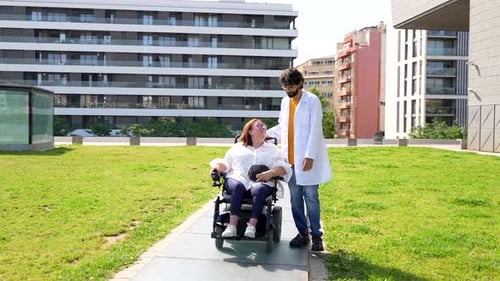 Doctor assisting happy disabled woman in wheelchair in city park