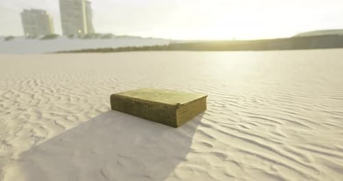 Old Book Resting on Sandy Beach at Sunset Near Distant Buildings