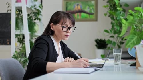 Geschäftsfrau mittleren Alters, die im Heimbüro mit Laptop arbeitet und Notizen macht
