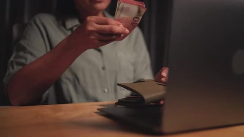 Sitting counting money while working at computer on desk during economic downturn